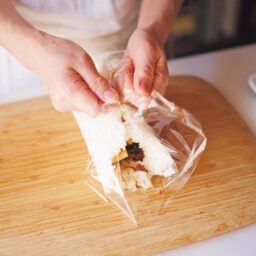 ラップごと持ち上げ、ごはんの左右の端をくっつけて閉じる