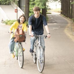 映画『佐藤さんと佐藤さん』より自転車に乗りながら歌うサチ（岸井ゆきの）とタモツ（宮沢氷魚）