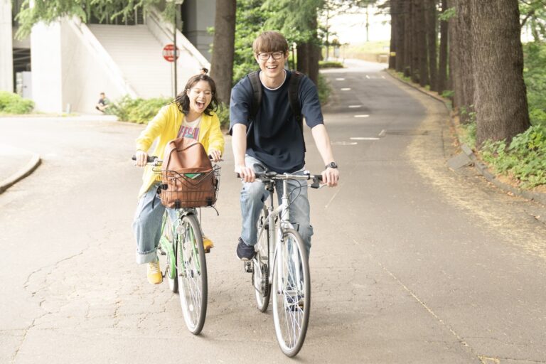 映画『佐藤さんと佐藤さん』より自転車に乗りながら歌うサチ（岸井ゆきの）とタモツ（宮沢氷魚）