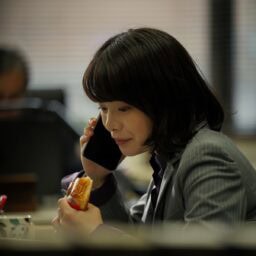 映画『佐藤さんと佐藤さん』よりデスクでパンをほおばるサチ（岸井ゆきの）