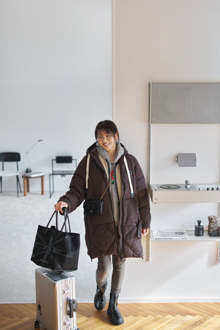 中綿コート、リバーシブルベスト／ともにオットダム、フーディ／グッチ、パンツ／カリアング、ピアス／ヴァンクリーフ＆アーペル、ポシェット／ローレン ラルフ ローレン、バッグ／A.D.M.J.、スーツケース／リモワ、ブーツ／ノーネーム（すべて私物）