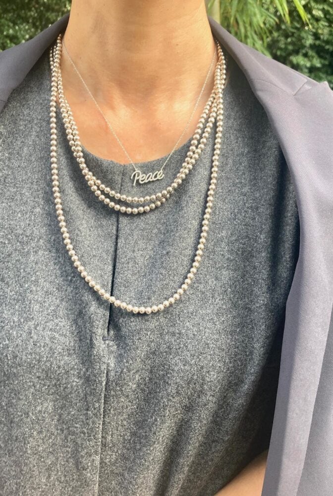 シルバーカラーのレターペンダントと、クラシックな3連パールを重ね付け。