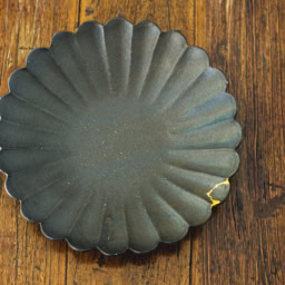 黒釉の輪花皿は高島大樹さんの作品のなかでも、人気の逸品。「希少な器なのに欠けてしまって、金継ぎに出しました。ヒビの風情もお気に入りです」