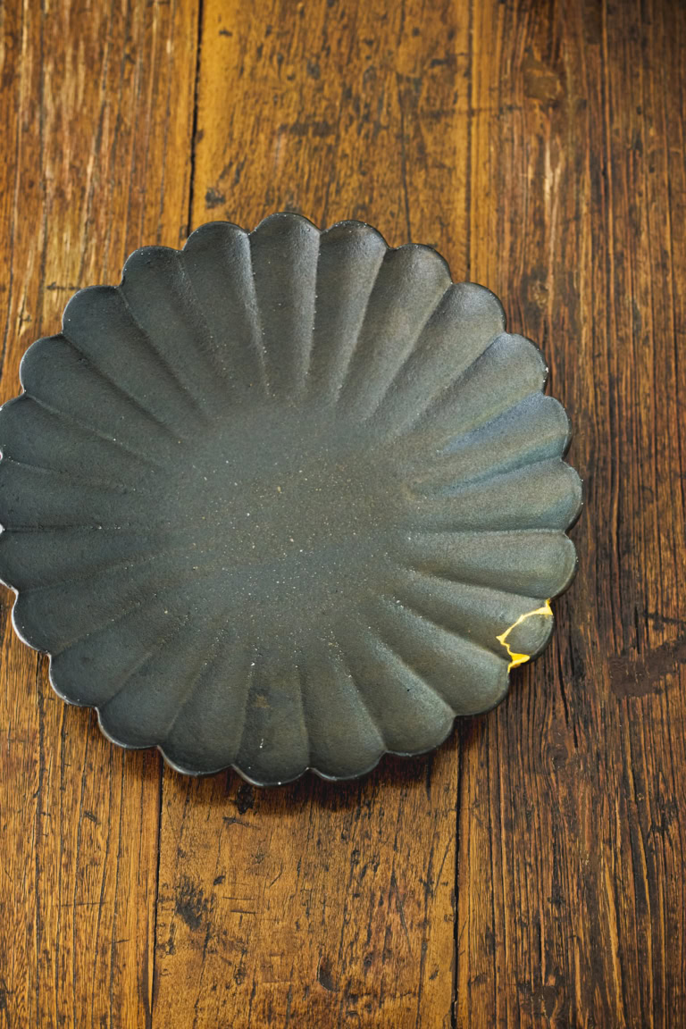 黒釉の輪花皿は高島大樹さんの作品のなかでも、人気の逸品。「希少な器なのに欠けてしまって、金継ぎに出しました。ヒビの風情もお気に入りです」