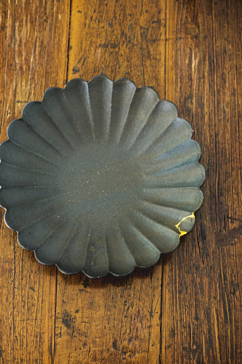 黒釉の輪花皿は高島大樹さんの作品のなかでも、人気の逸品。「希少な器なのに欠けてしまって、金継ぎに出しました。ヒビの風情もお気に入りです」