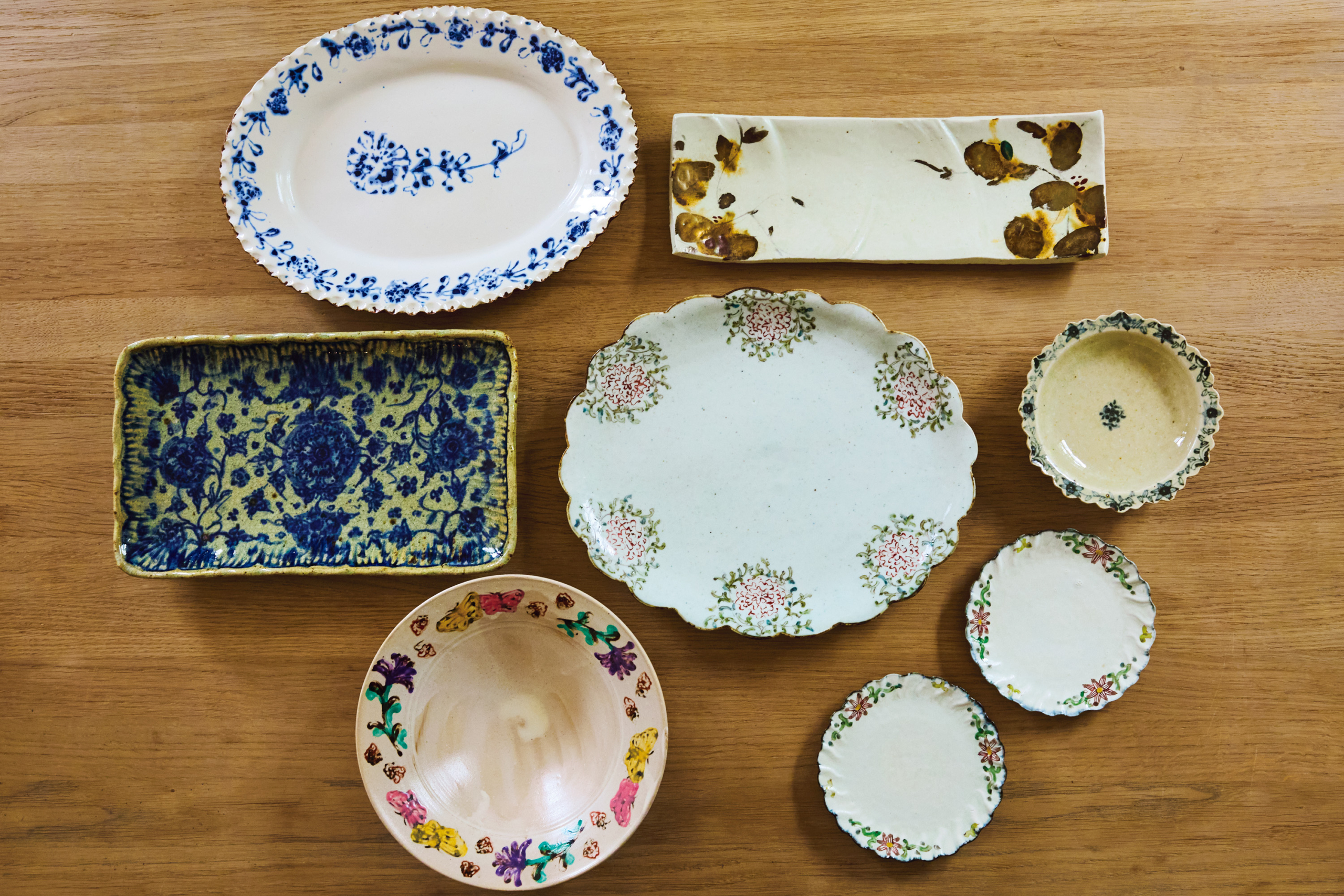 左上から時計まわりに、白地にブルーの花が映える伊藤聡信(あきのぶ)さんの印判皿。シックな長皿とリムに花をあしらった丸皿3枚は「天平窯」のもの。「岡晋吾さん、さつきさんご夫婦による窯で、長皿は晋吾さん、丸皿はさつきさんの作品です。もともと母が好きで私も20年以上前から集めています。やさしい筆運びが素敵でしょう?」。蝶々柄の鉢はヨシノヒトシさん、ブルーの花が咲き誇る長皿はイムサエムさんのもの。「イムサエムさんの器は少々重いものの、料理映えがすごい!昨年引退され、もう新作が見られないと思うと寂しいですね」。中央の楕円皿も「天平窯」のもの。