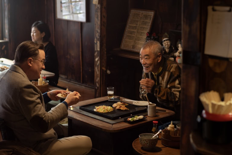 映画『レンタル・ファミリー』よりお好み焼きを食べる大御所俳優・長谷川喜久雄（柄本明）とフィリップ（ブレンダン・フレイザー）