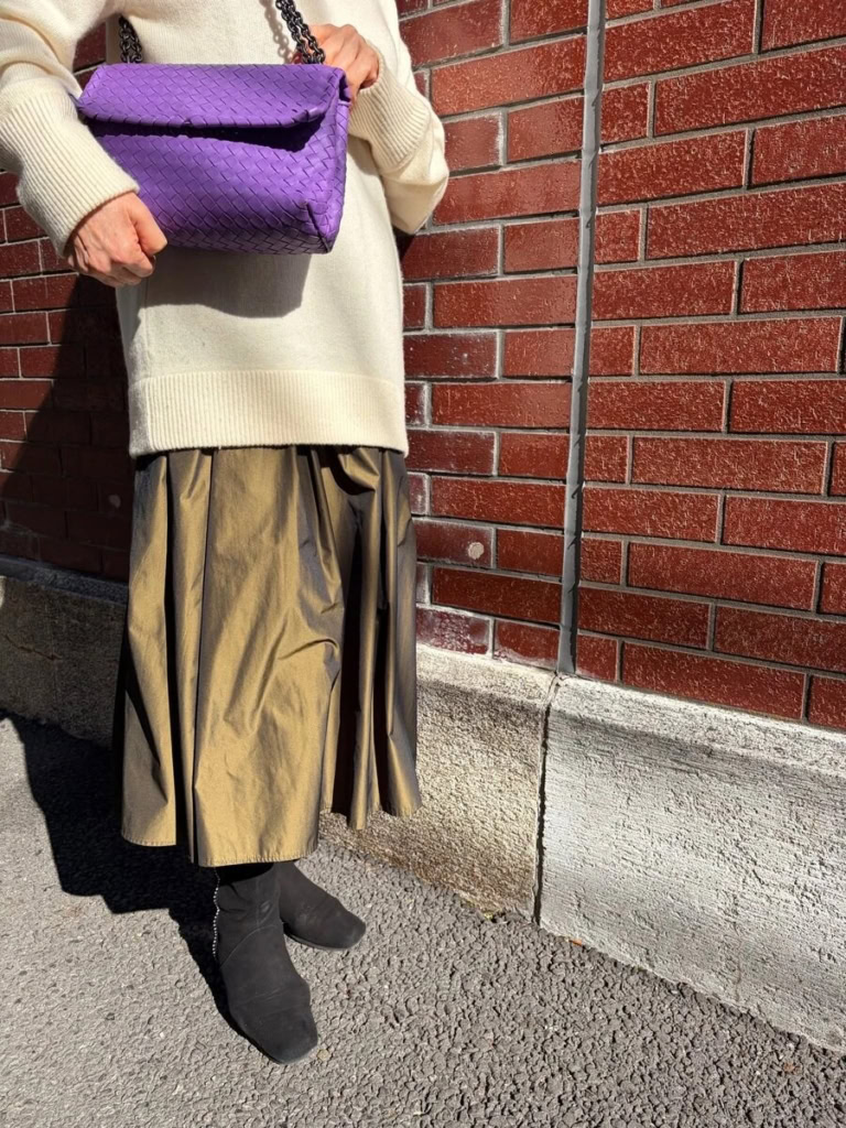 光を含んだようなツヤが、動くたびに表情を変えるロングスカートは「シビラ」。「ヴェイク」のカシミヤ100%ニットは、極上の柔らかさと暖かさが好きなのだそう。「ヒップが隠れる長さのニットなので、パンツでも良かったのですが、”ゆるっと大人かわいい”というテーマにしたかったので、あえてロングスカートとあわせて優しい印象にしました」