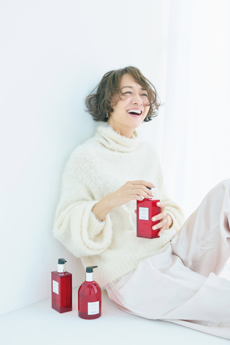 〈床置き右から〉「オー ドゥ ルバーブ エルカラット」ハンド&ボディ クレンジングジェル¥11,110、同 ヘア&ボディ シャワージェル¥11,000、〈手に持ったボトル〉同 モイスチャライジング ボディローション¥12,650/すべてエルメス(エルメスジャポン)、ニット¥39,600/カオス(Chaos GINZA SIX)、パンツ※参考商品/デパリエ(デパリエ 伊勢丹新宿店)、ピアス¥40,000/トムウッド(トムウッド 青山店)