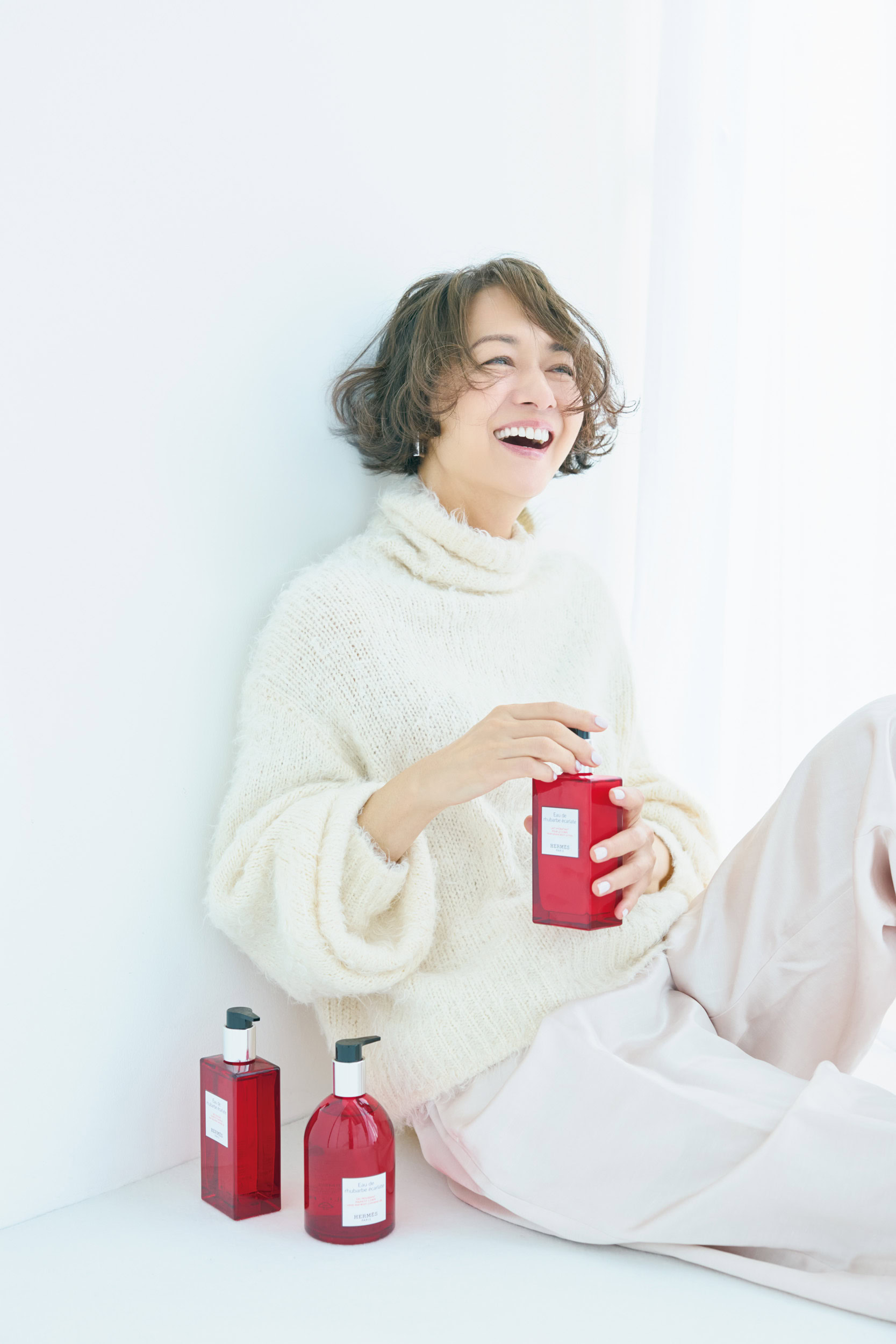 〈床置き右から〉「オー ドゥ ルバーブ エルカラット」ハンド＆ボディ クレンジングジェル¥11,110、同 ヘア＆ボディ シャワージェル¥11,000、〈手に持ったボトル〉同 モイスチャライジング ボディローション¥12,650／すべてエルメス（エルメスジャポン）、ニット¥39,600／カオス（Chaos GINZA SIX）、パンツ※参考商品／デパリエ（デパリエ 伊勢丹新宿店）、ピアス¥40,000／トムウッド（トムウッド 青山店）