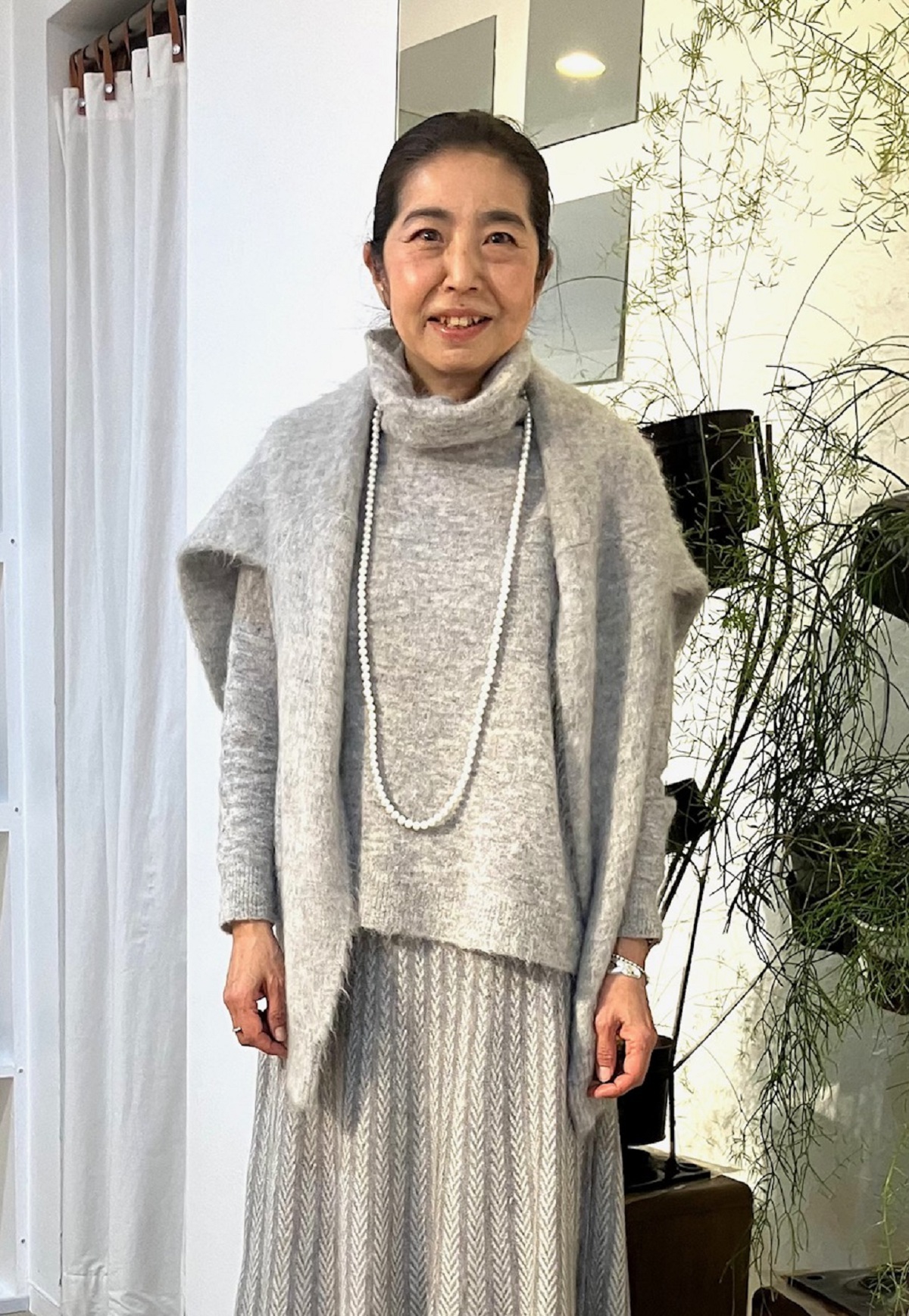 「グレーのワントーンスタイルでまとめました」と三好さん。「ワントーンコーデは、すっきり見せしてくれるので、バランスがまとまりやすいのですが、単調になってしまう場合もあるので、柄物スカートやニットカーディガンなどをアクセントに」。肩掛けしたニットとスカートは、ル シェル ド ハリス。同系色のオフタートルニットはベラ ジョーンズのもの。ハリスのパールロングネックレスをオン。